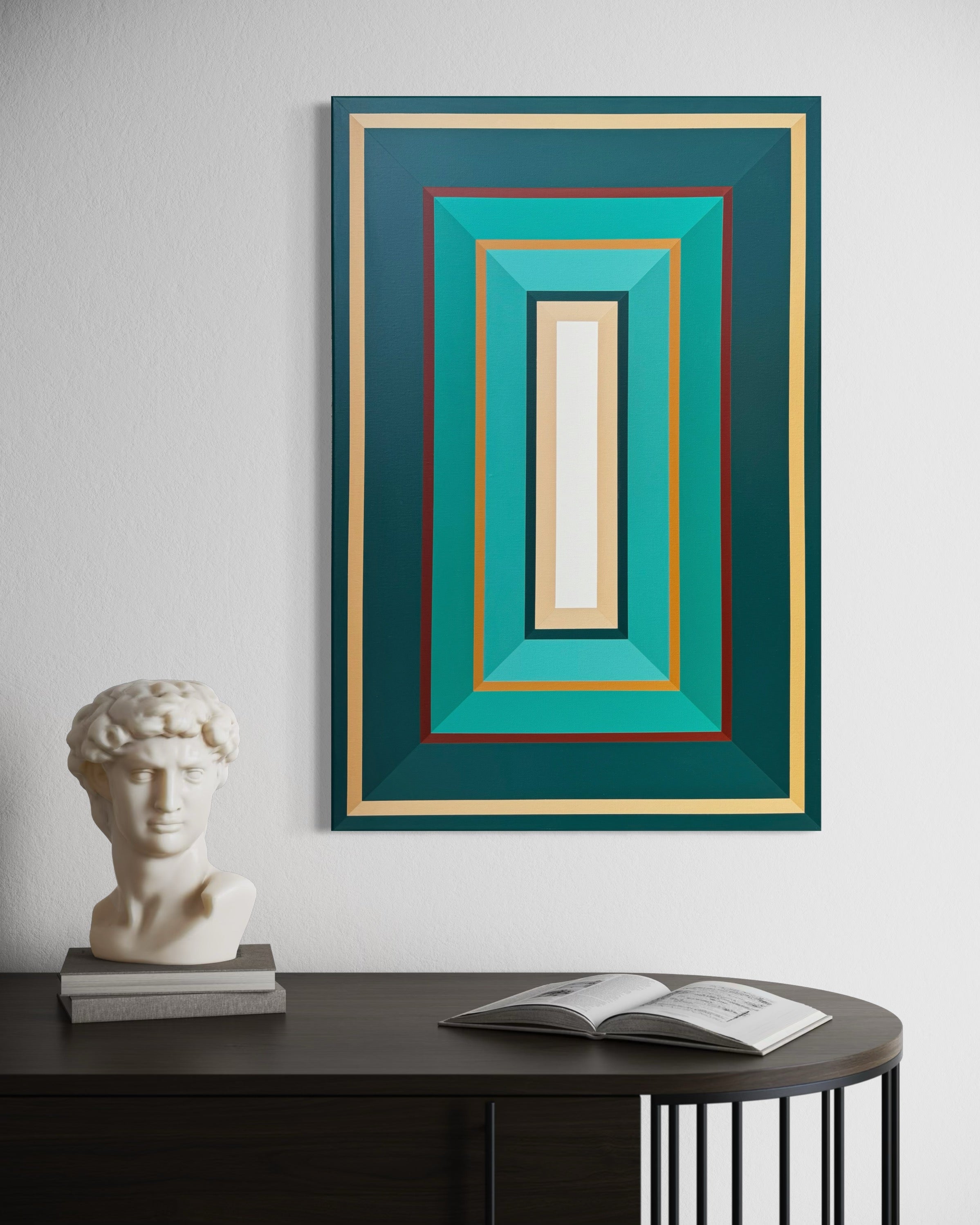 Framed abstract artwork with geometric design on a wall above a table with a sculpture and book.