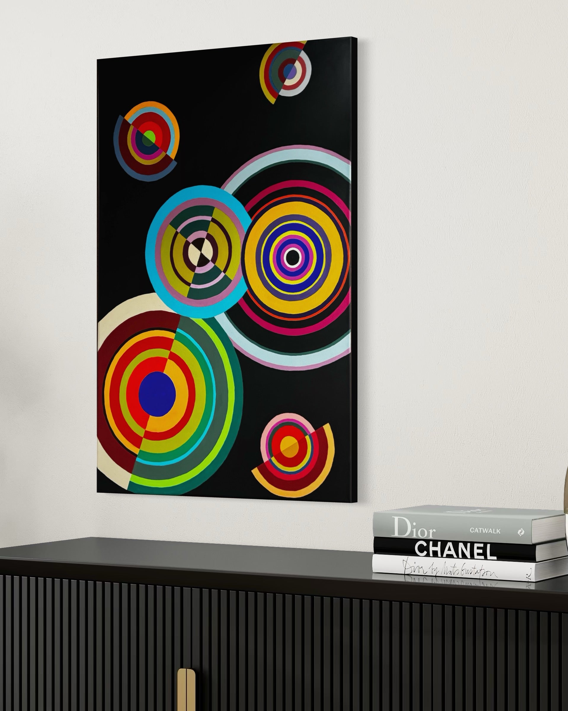 Abstract art piece with colorful circles on a black background, displayed on a wall above a black cabinet.