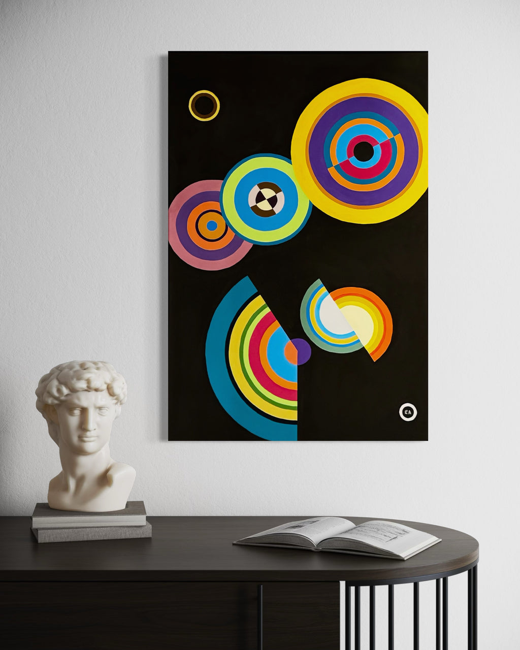 Colorful abstract art print on a wall above a table with a sculpture and book.