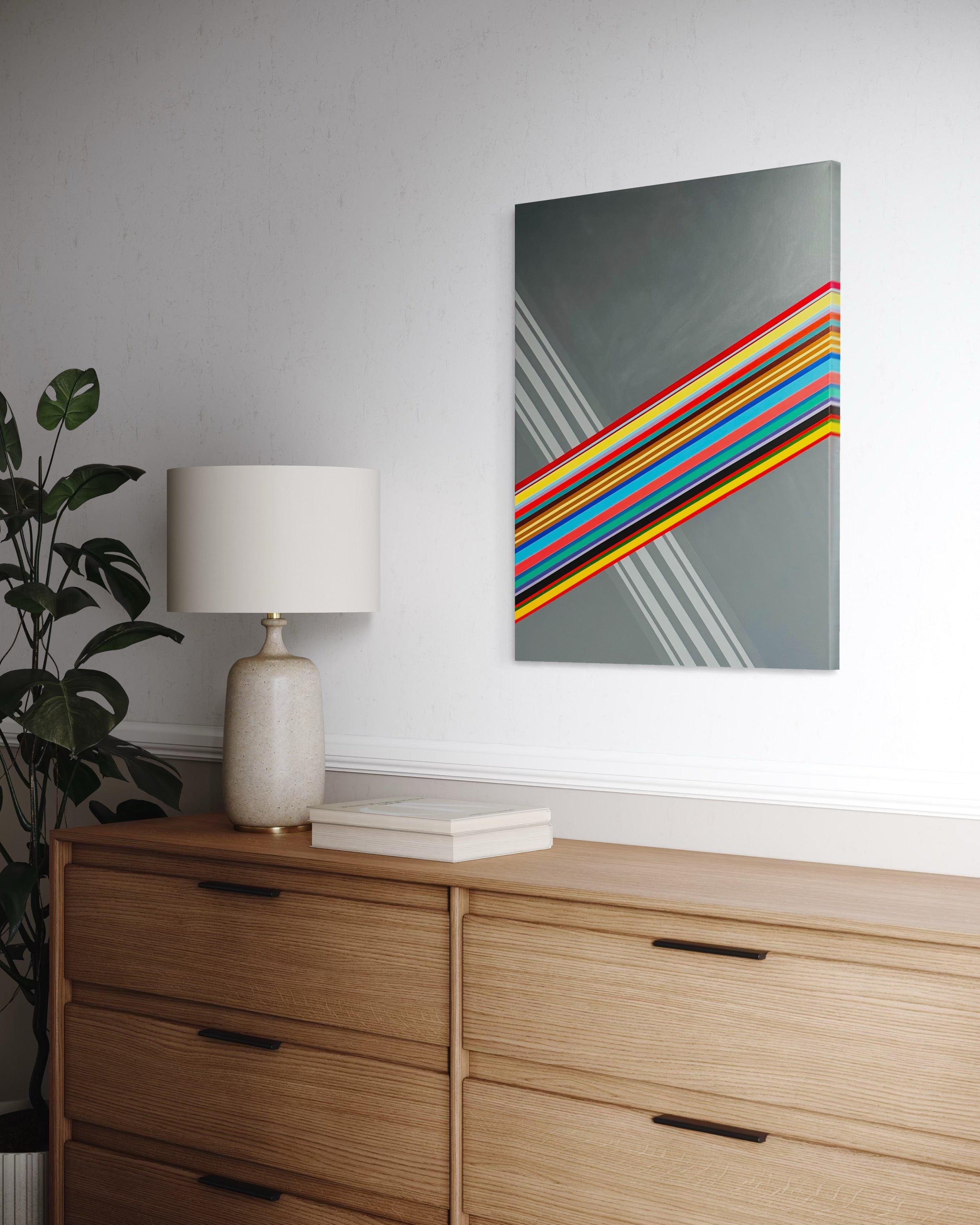 Colorful abstract painting on a wall above a wooden dresser with a lamp and plant.
