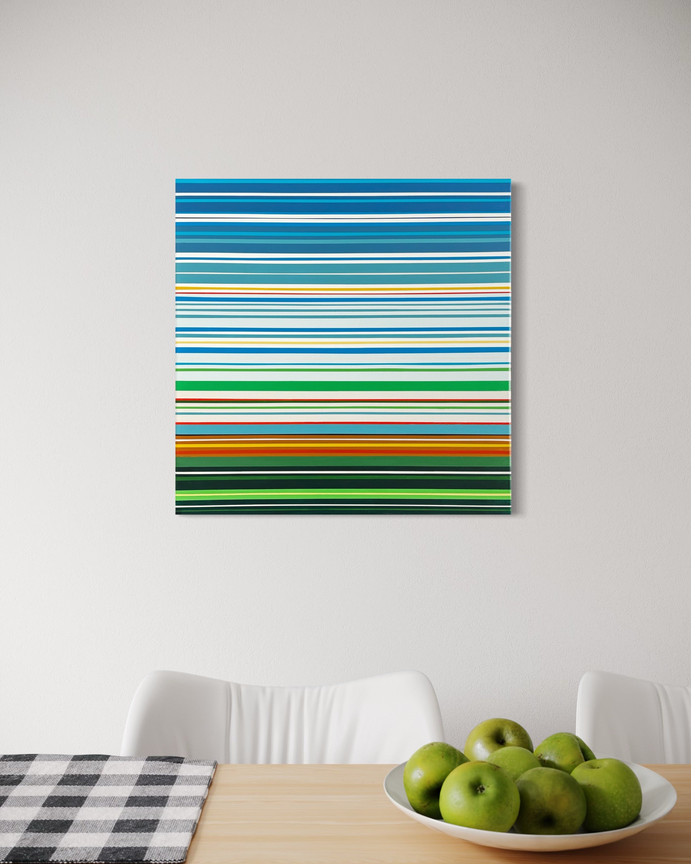Colorful striped painting on a white wall above a table with apples and a checkered cloth.