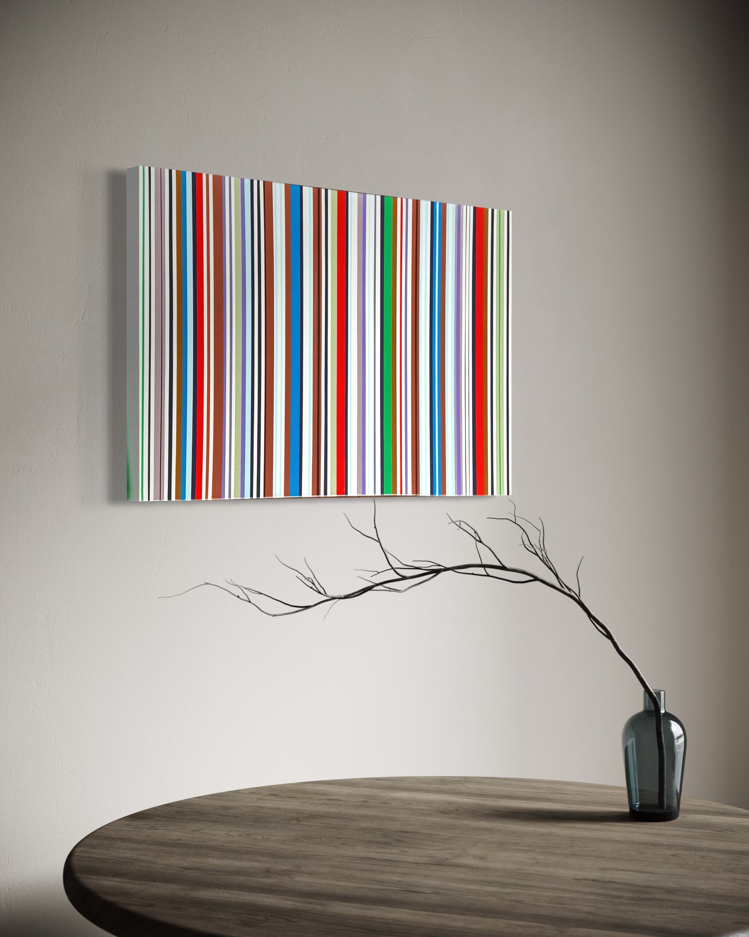 Colorful striped painting on a wall above a wooden table with a vase and branches.
