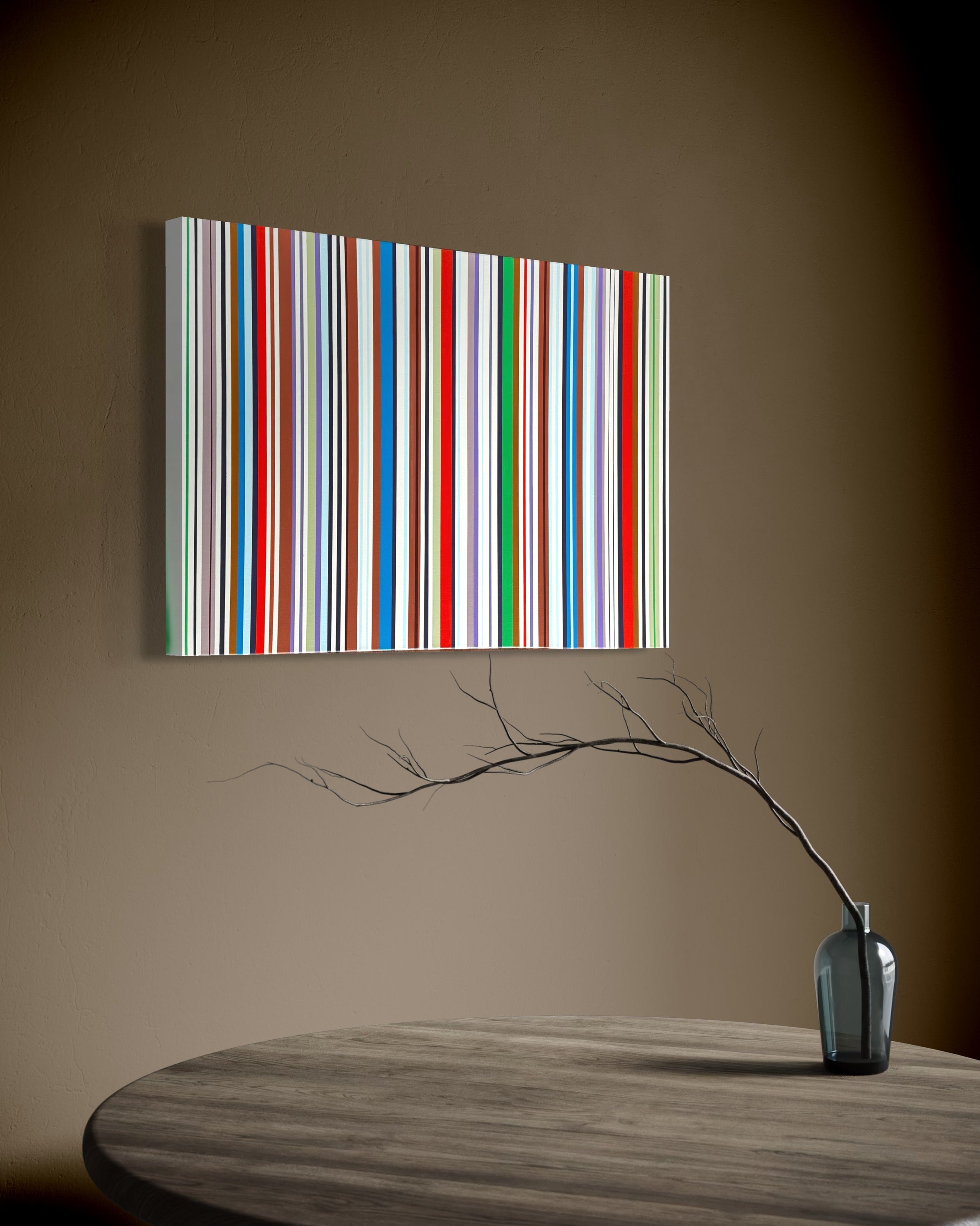 Colorful striped painting on a brown wall above a wooden table with a vase and branches.