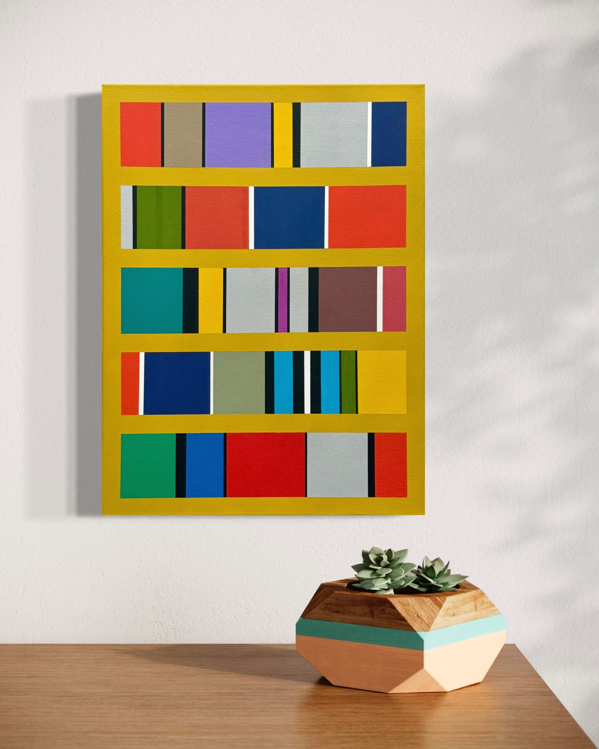 Colorful abstract wall art with a geometric design on a white wall, accompanied by a wooden planter with succulents on a wooden surface.