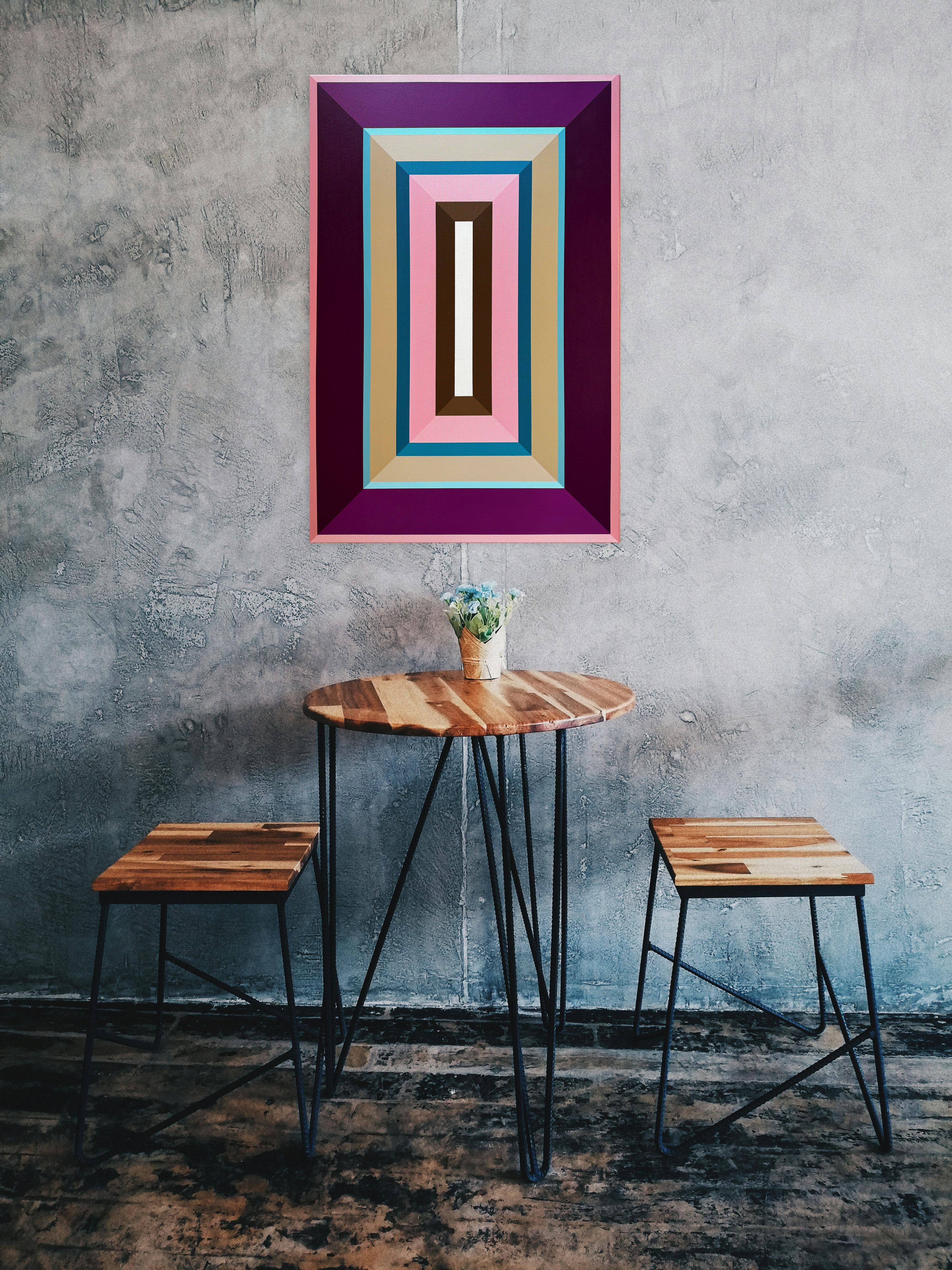 The vibrant "Pink-Bubble-Gum" painting adding a playful pop of color to an industrial-chic space, hung on a textured grey wall above a small wooden table.