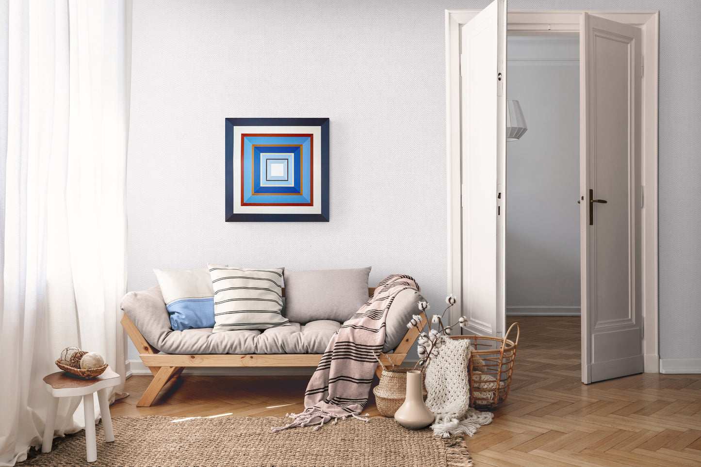 Hard edge painting 'Denim' by Elena Alexander featuring concentric squares in navy, brown, and blues. Shown in a cozy Scandinavian living space with daybed, natural textures, and neutral decor. Geometric wall art adds bold contrast to soft, organic elements.